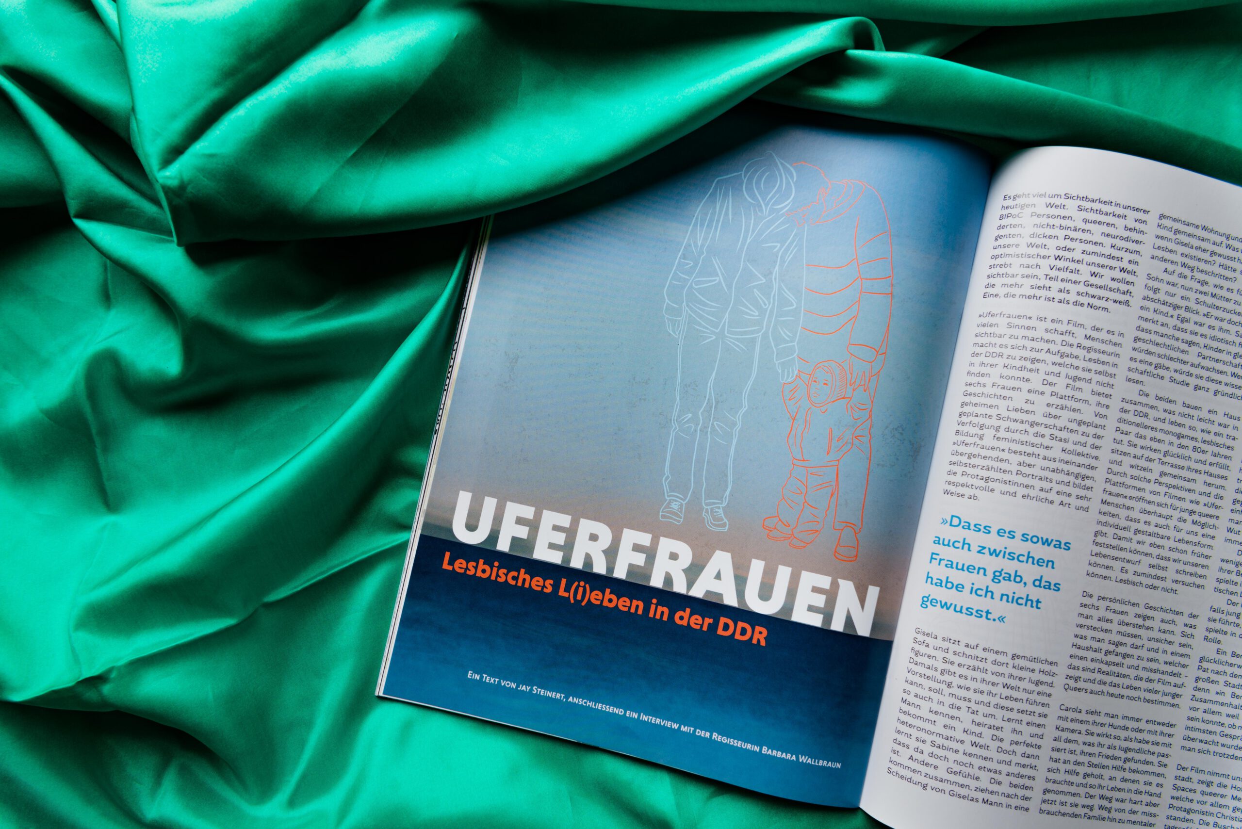 Das Magazin liegt geöffnet auf einem grünen Stoff. Auf der linken Seite ist der Text Uferfrauen auf blauem Hintergrund zu sehen. Rechts ist das Magazin schräg angeschnitten und zeigt den Beitragstext.