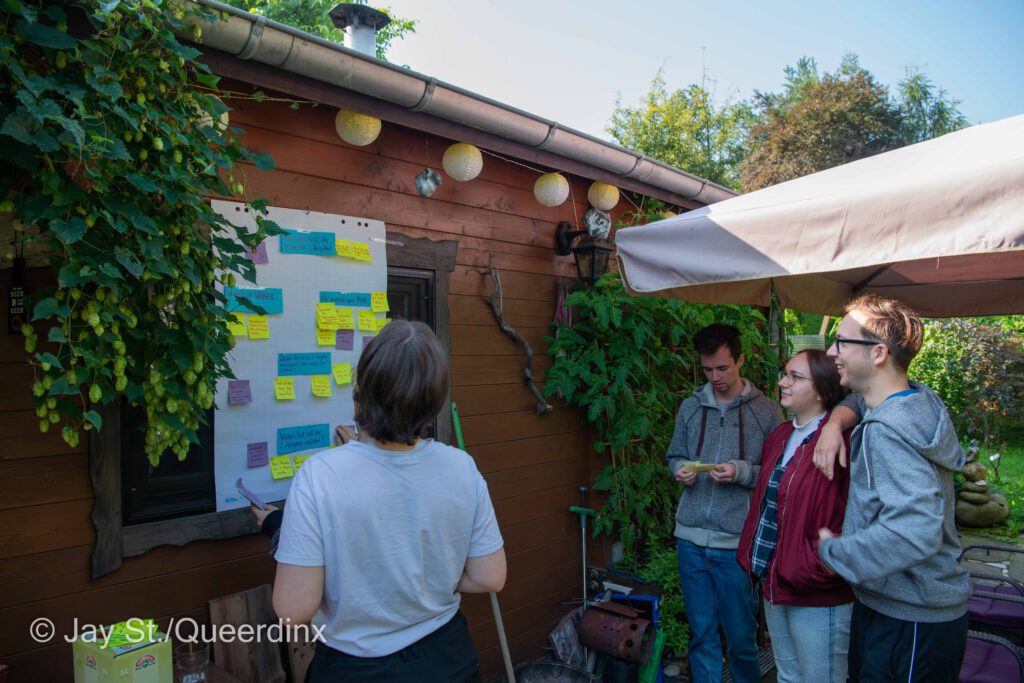 Vier Redaktionsmitglieder stehen vor dem improvisierten Whiteboard und schauen auf die Post-Its. 