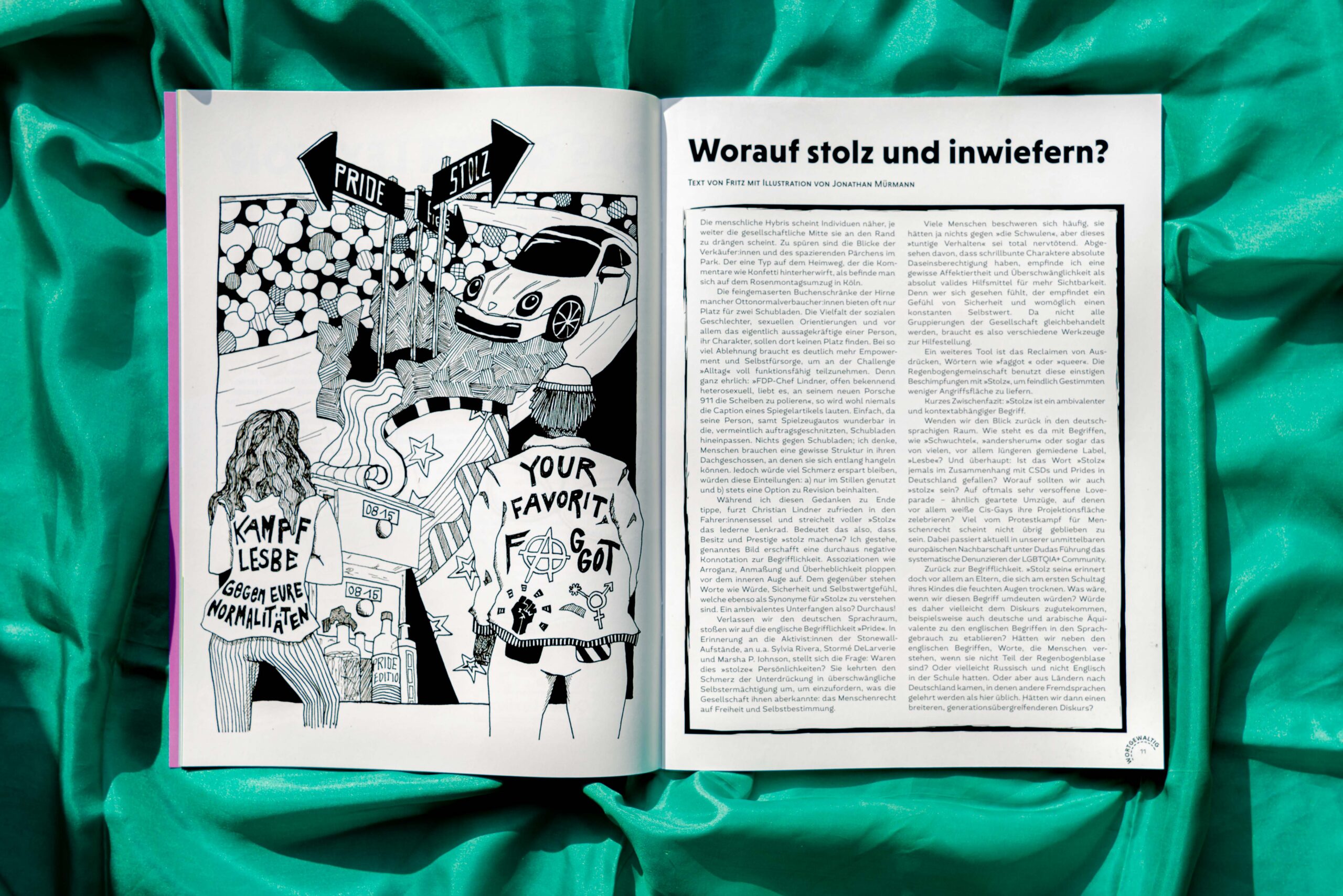 Das Magazin liegt geöffnet auf einem grünen Stoff. Auf der linken Seite ist eine schwarz-weiße Illustration, auf der rechten Seite steht die Überschrift "Worauf stolz und inwiefern?" mit einem eingerahmten Text darunter.