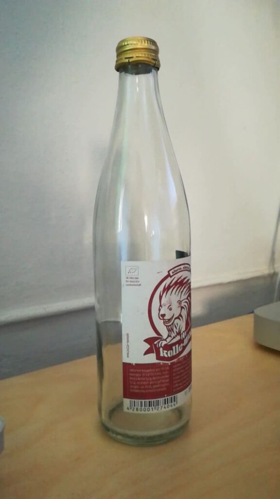 Eine leere Kolle-Mate Flasche steht auf einem Holztisch. 