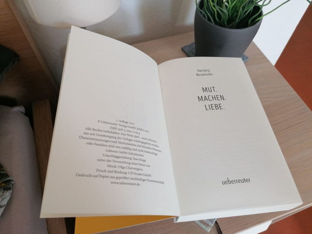 Das Buch "Mut.Machen.Liebe" liegt geöffnet auf einem Nachttisch. 